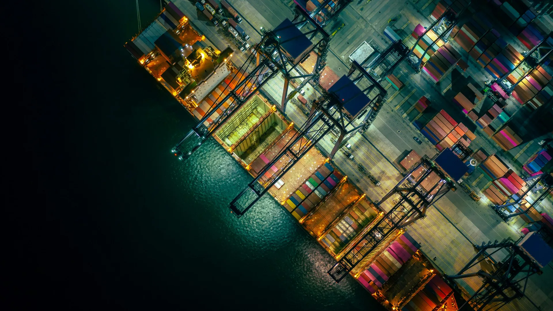 Vista aérea noturna de terminal portuário com navio porta-contêineres sendo operado por guindastes